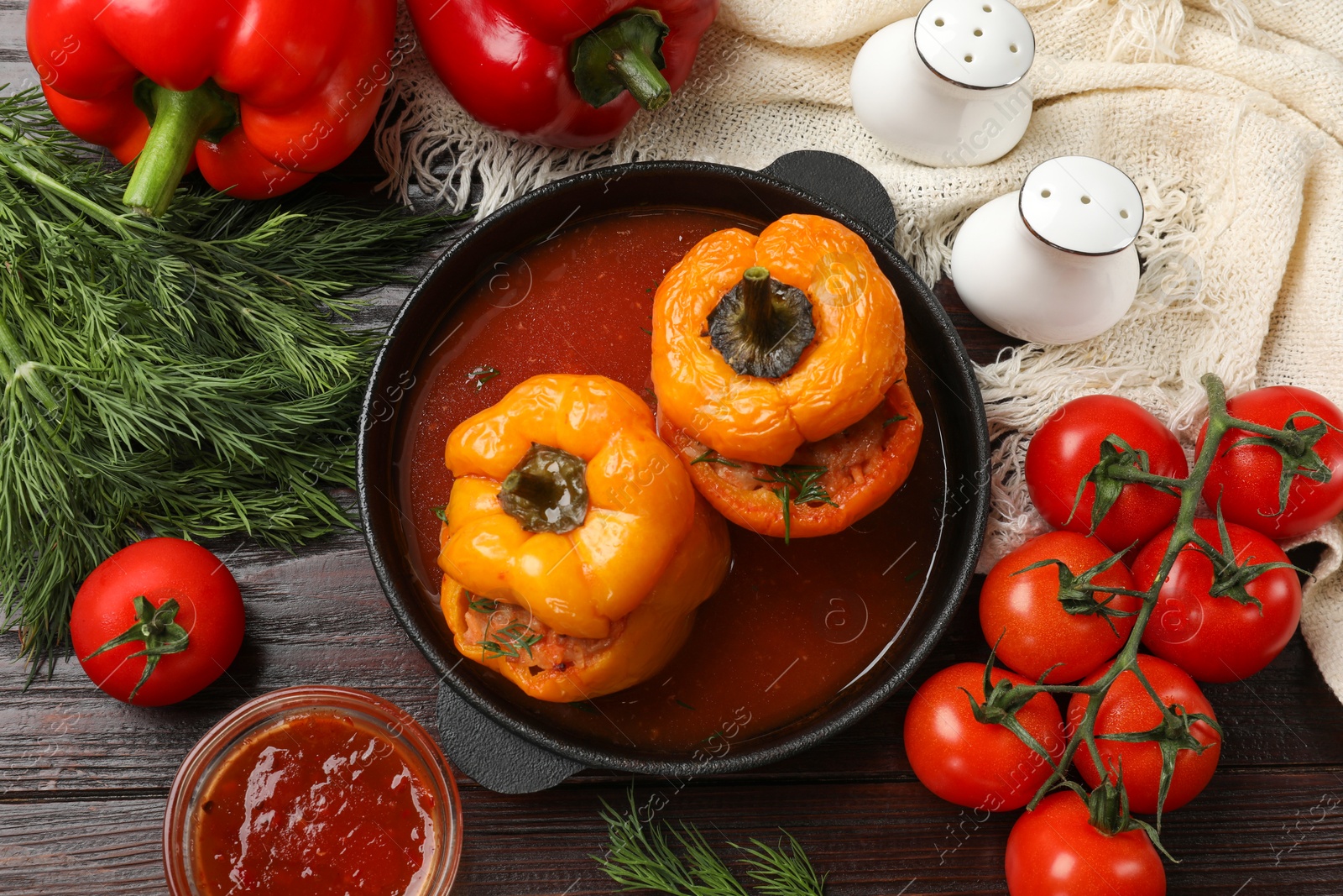 Photo of Tasty stuffed peppers in pan, sauce and products on wooden table, flat lay