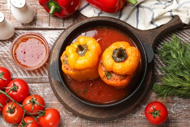 Photo of Tasty stuffed peppers in pan, sauce and products on wooden rustic table, flat lay