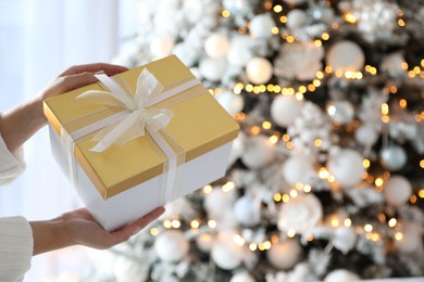 Photo of Woman holding gift box near Christmas tree. Festive interior