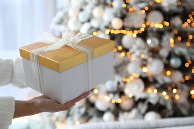 Photo of Woman holding gift box near Christmas tree. Festive interior