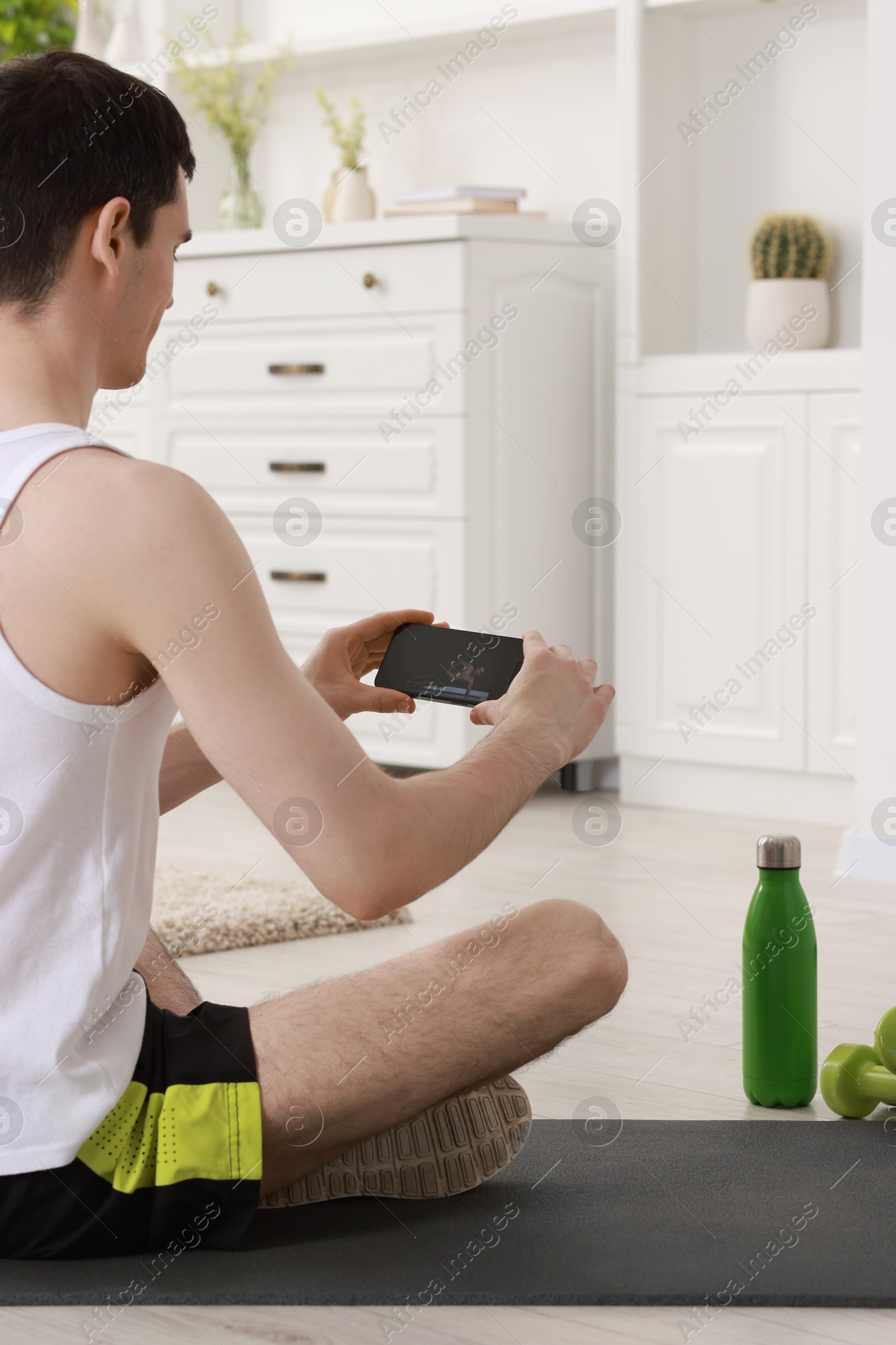 Photo of Online fitness trainer. Man watching tutorial on smartphone at home