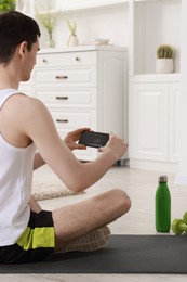 Photo of Online fitness trainer. Man watching tutorial on smartphone at home