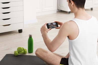 Photo of Online fitness trainer. Man watching tutorial on smartphone at home, closeup
