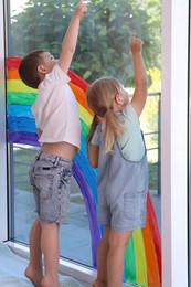 Photo of Children touching picture of rainbow on window indoors