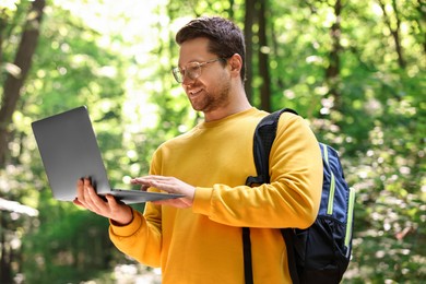 Smiling traveler working with laptop outdoors on sunny day. Remote job