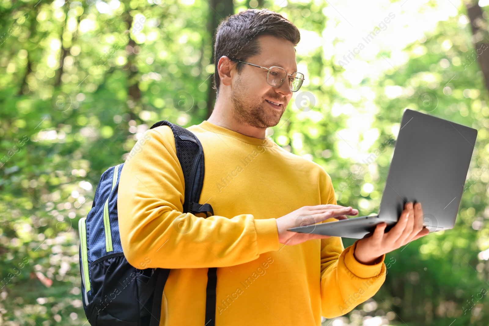 Photo of Smiling traveler working with laptop outdoors on sunny day. Remote job