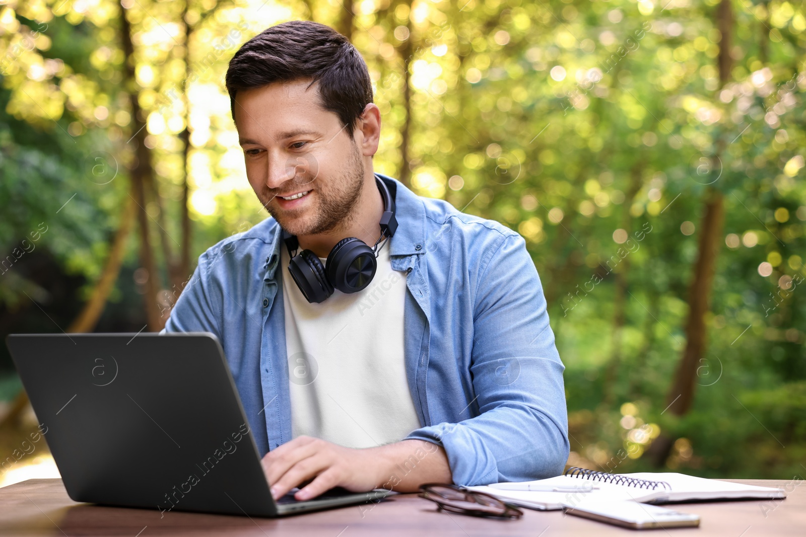 Photo of Smiling freelancer working with laptop at table outdoors. Remote job