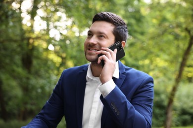Photo of Smiling businessman talking on smartphone in park. Remote job