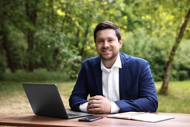 Smiling businessman working with laptop at table outdoors. Remote job