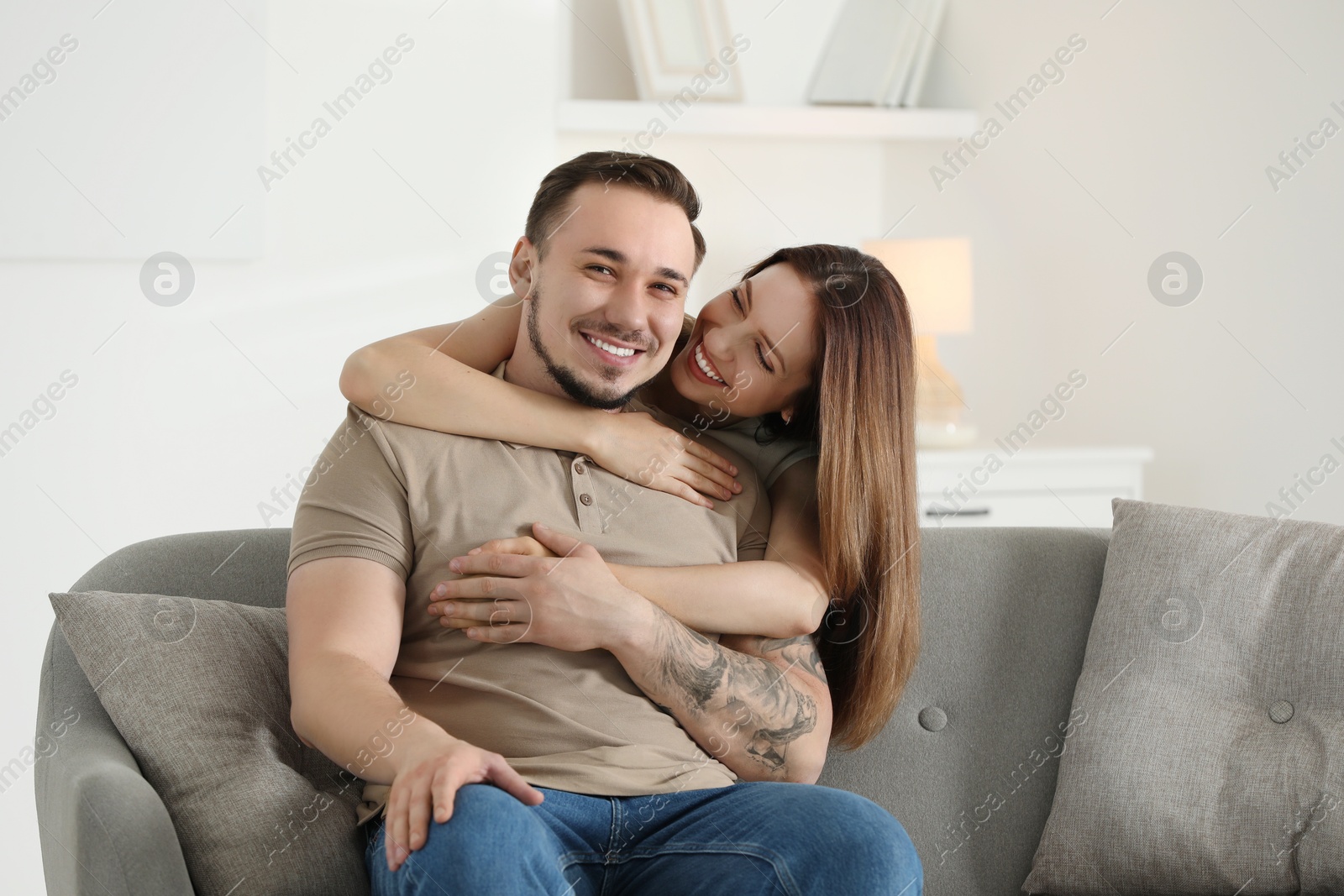 Photo of Woman hugging her happy boyfriend on sofa at home