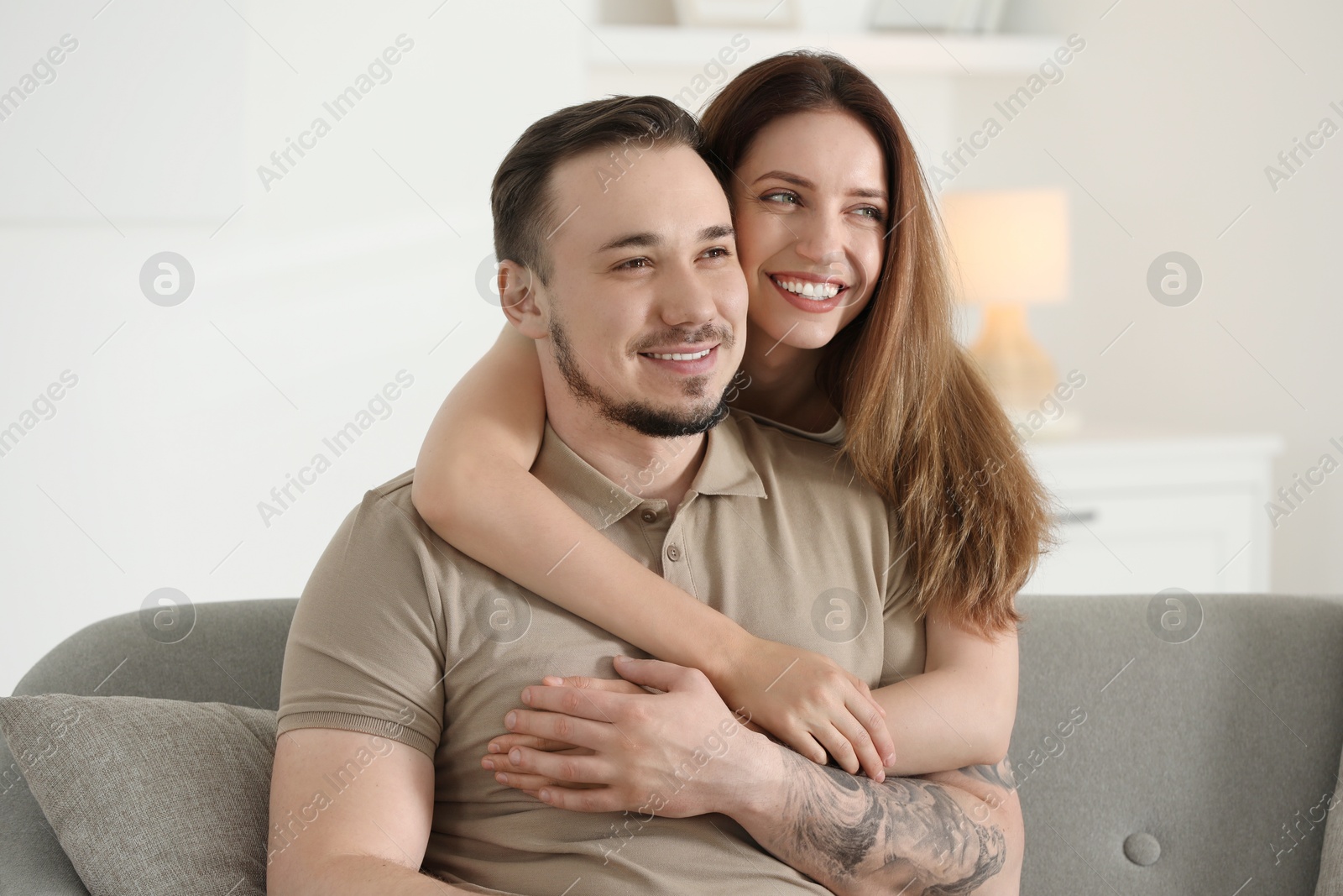 Photo of Woman hugging her happy boyfriend on sofa at home