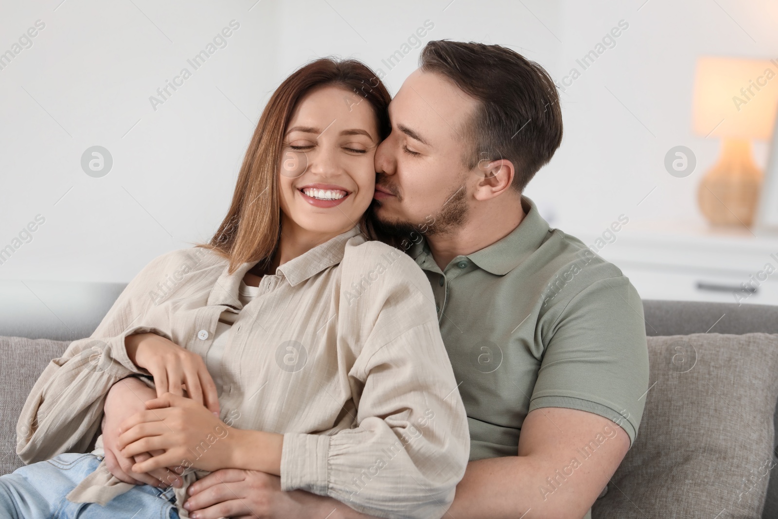 Photo of Man kissing his happy girlfriend on sofa at home