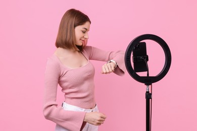 Photo of Fashion blogger reviewing watch and recording video with smartphone and ring lamp on pink background