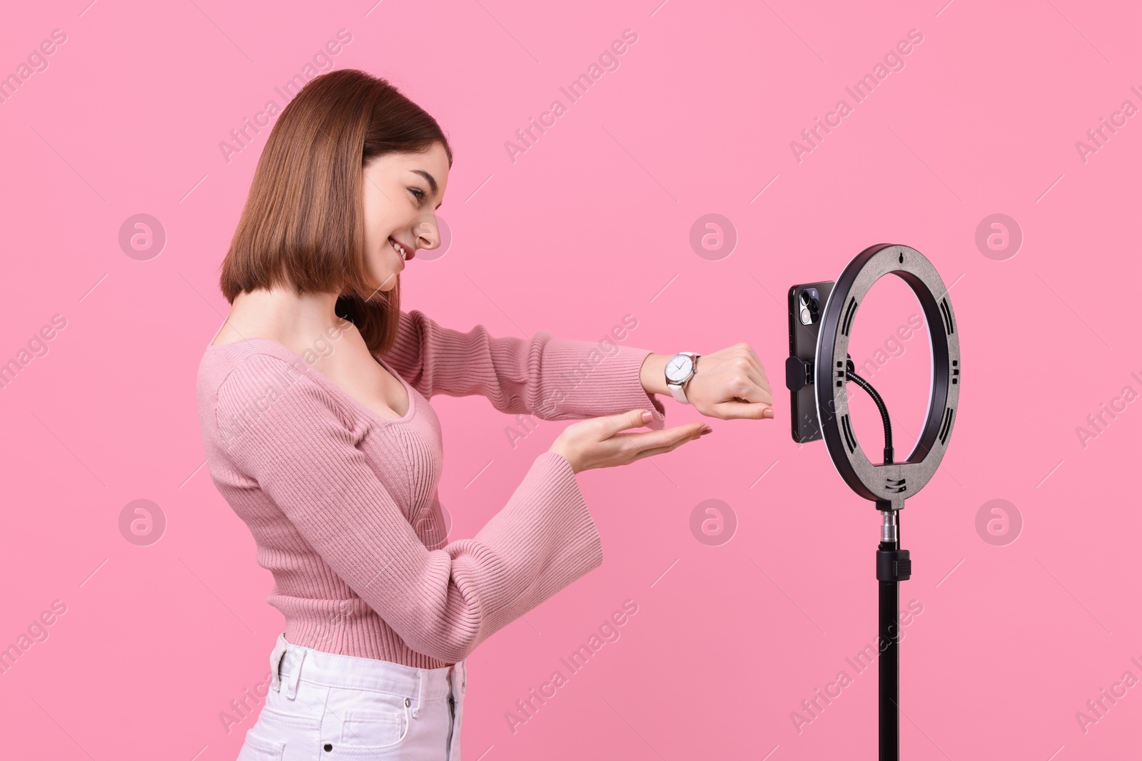 Photo of Fashion blogger reviewing watch and recording video with smartphone and ring lamp on pink background