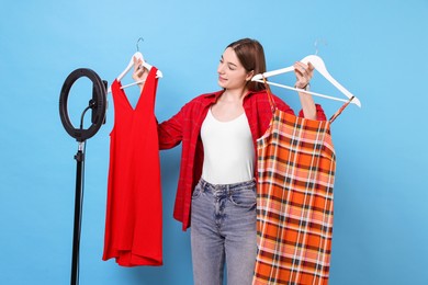 Photo of Fashion blogger reviewing dresses and recording video with smartphone and ring lamp on light blue background