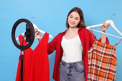 Fashion blogger reviewing dresses and recording video with smartphone and ring lamp on light blue background