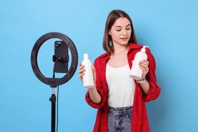 Beauty blogger reviewing cosmetic products and recording video with smartphone and ring lamp on light blue background
