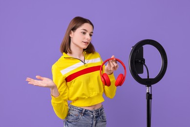 Technology blogger reviewing headphones and recording video with smartphone and ring lamp on purple background