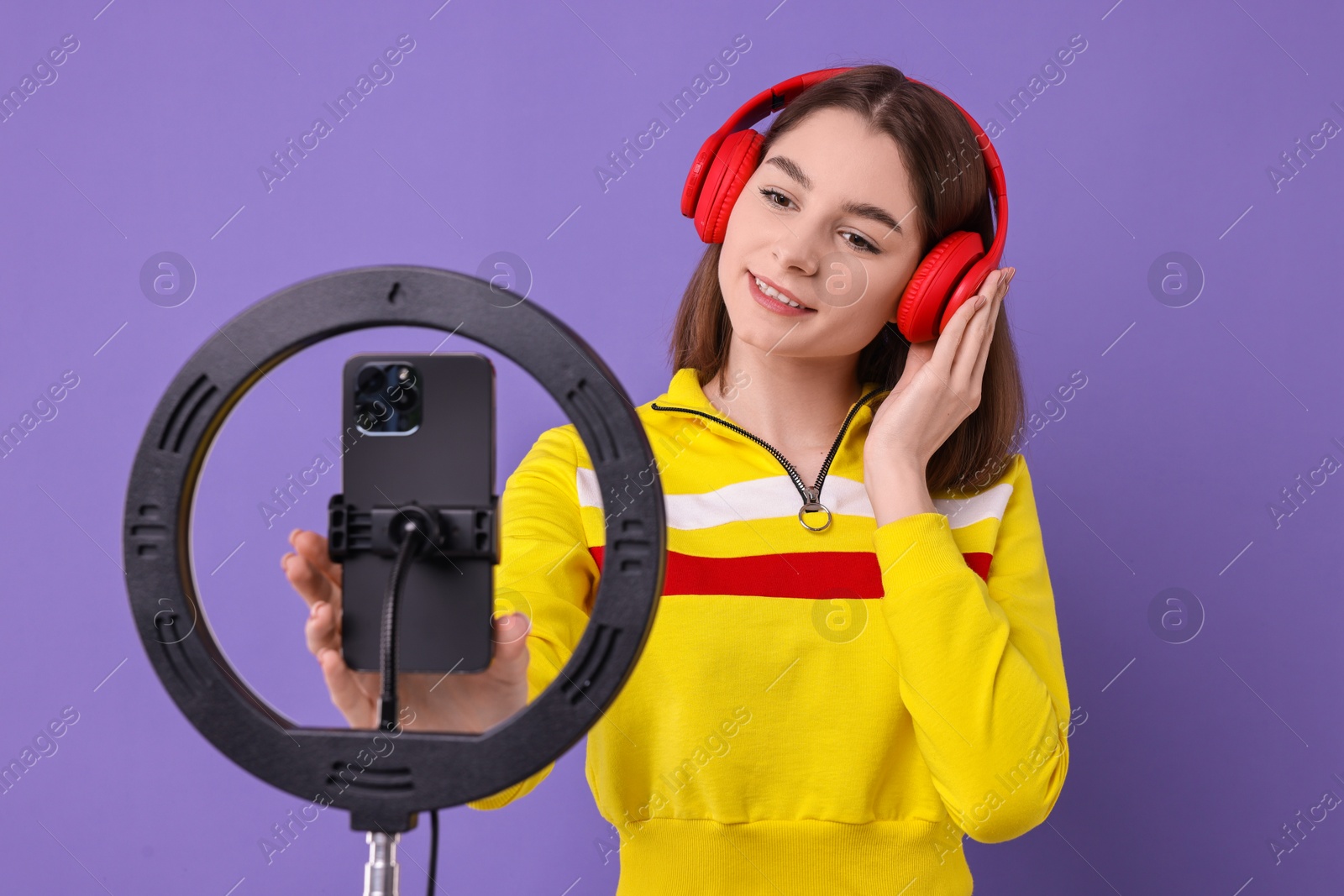 Photo of Technology blogger reviewing headphones and recording video with smartphone and ring lamp on purple background