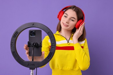 Technology blogger reviewing headphones and recording video with smartphone and ring lamp on purple background