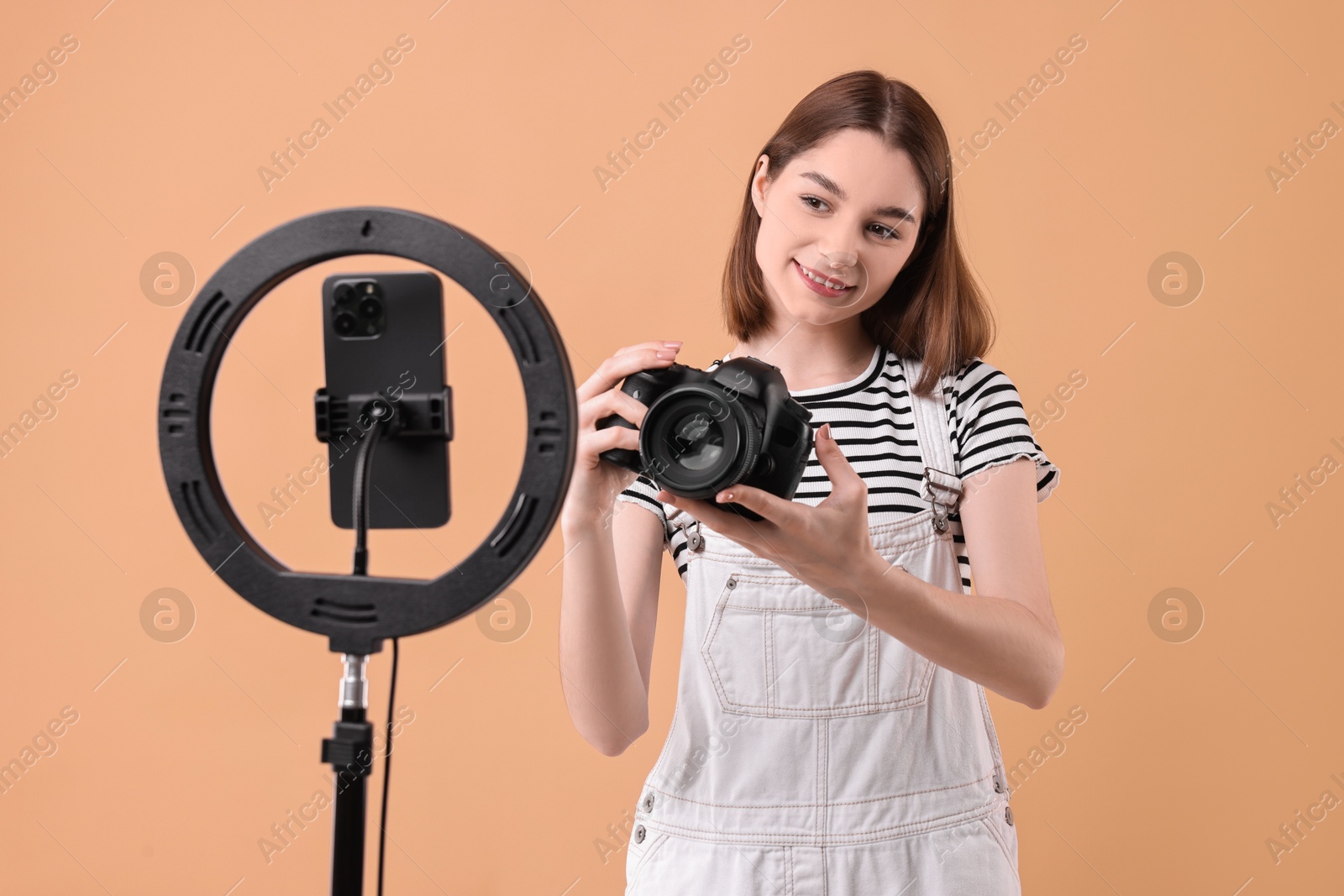 Photo of Technology blogger reviewing camera and recording video with smartphone and ring lamp on beige background