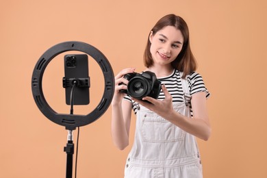 Technology blogger reviewing camera and recording video with smartphone and ring lamp on beige background