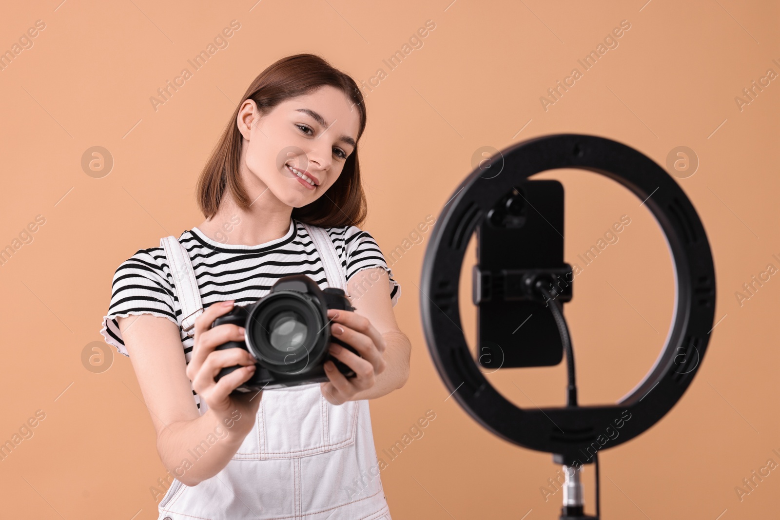 Photo of Technology blogger reviewing camera and recording video with smartphone and ring lamp on beige background