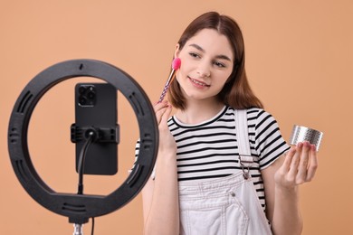 Photo of Beauty blogger reviewing decorative cosmetic product and recording video with smartphone and ring lamp on beige background