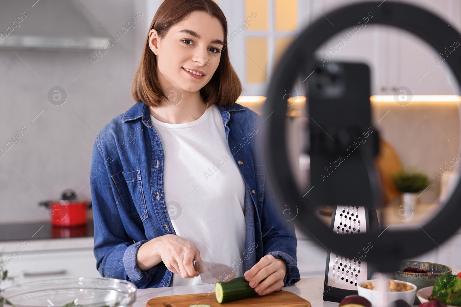 Photo of Food blogger cooking while recording video with smartphone and ring lamp in kitchen