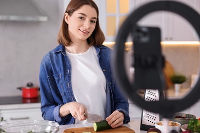 Food blogger cooking while recording video with smartphone and ring lamp in kitchen