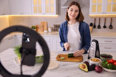 Food blogger cooking while recording video with smartphone and ring lamp in kitchen