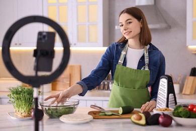 Food blogger cooking while recording video with smartphone and ring lamp in kitchen