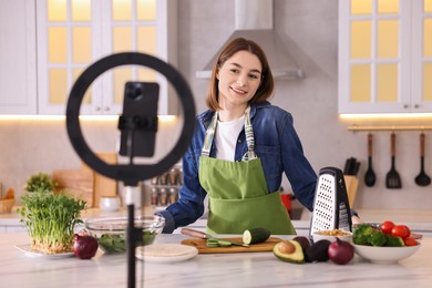 Food blogger cooking while recording video with smartphone and ring lamp in kitchen