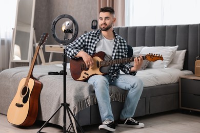 Music blogger recording guitar lesson with smartphone and ring lamp at home