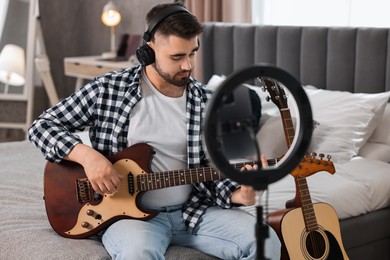 Photo of Music blogger recording guitar lesson with smartphone and ring lamp at home