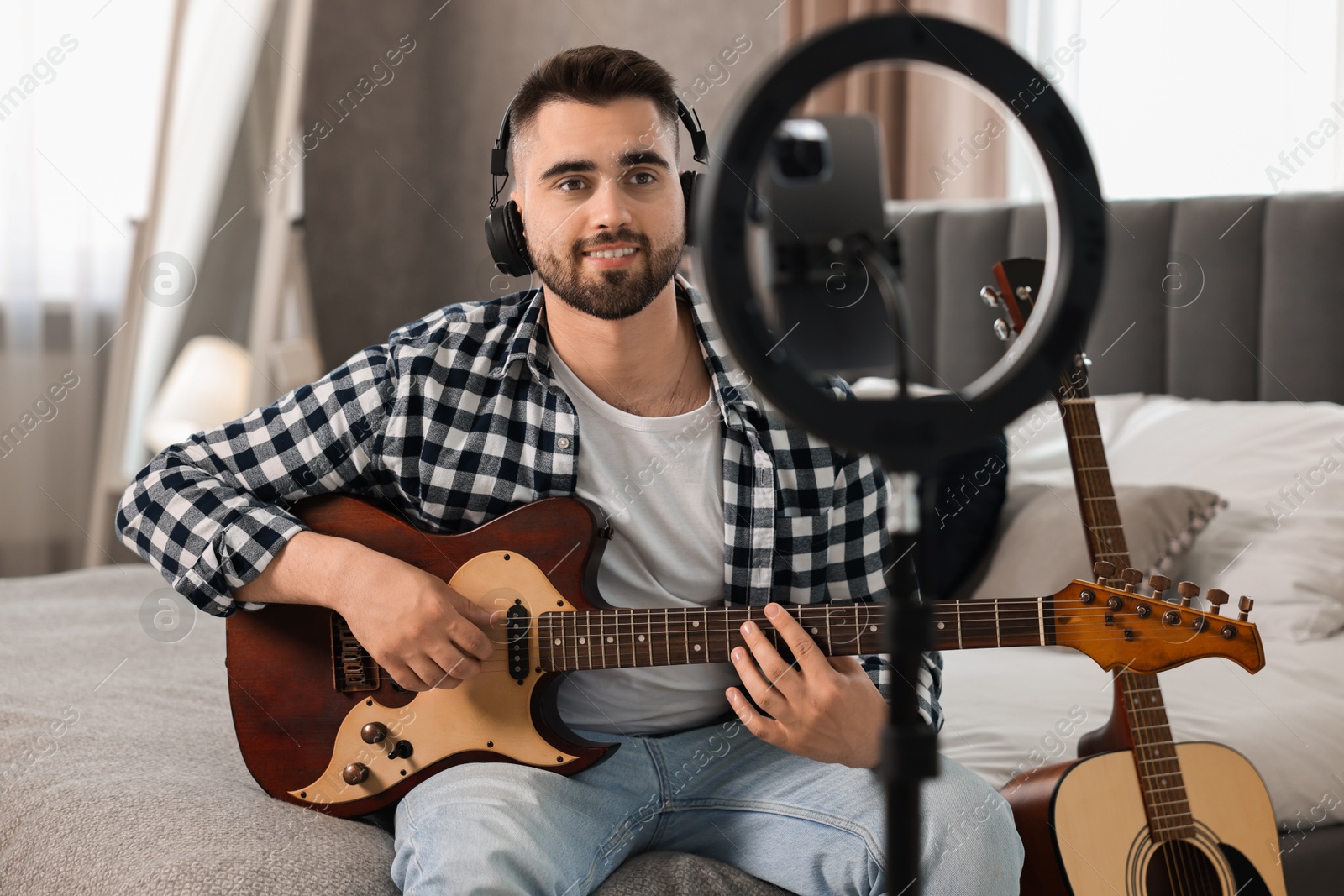 Photo of Music blogger recording guitar lesson with smartphone and ring lamp at home