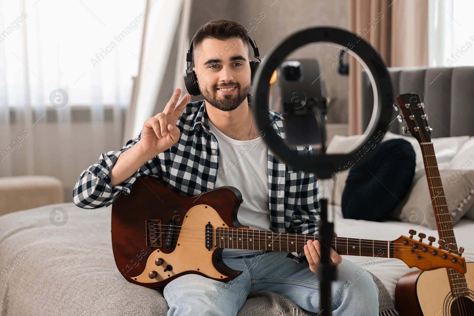 Photo of Music blogger recording guitar lesson with smartphone and ring lamp at home