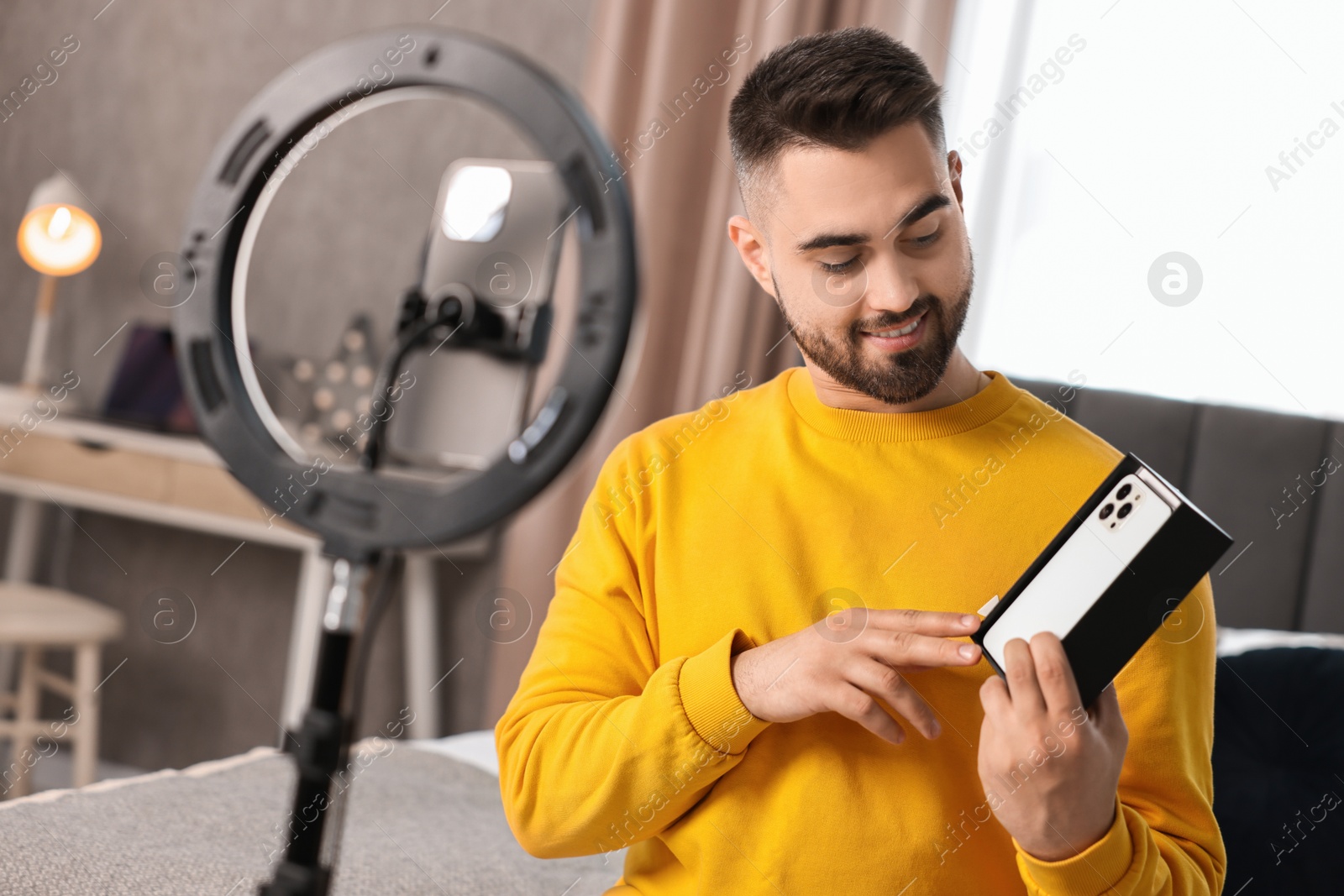 Photo of Technology blogger reviewing phone and recording video with smartphone and ring lamp at home