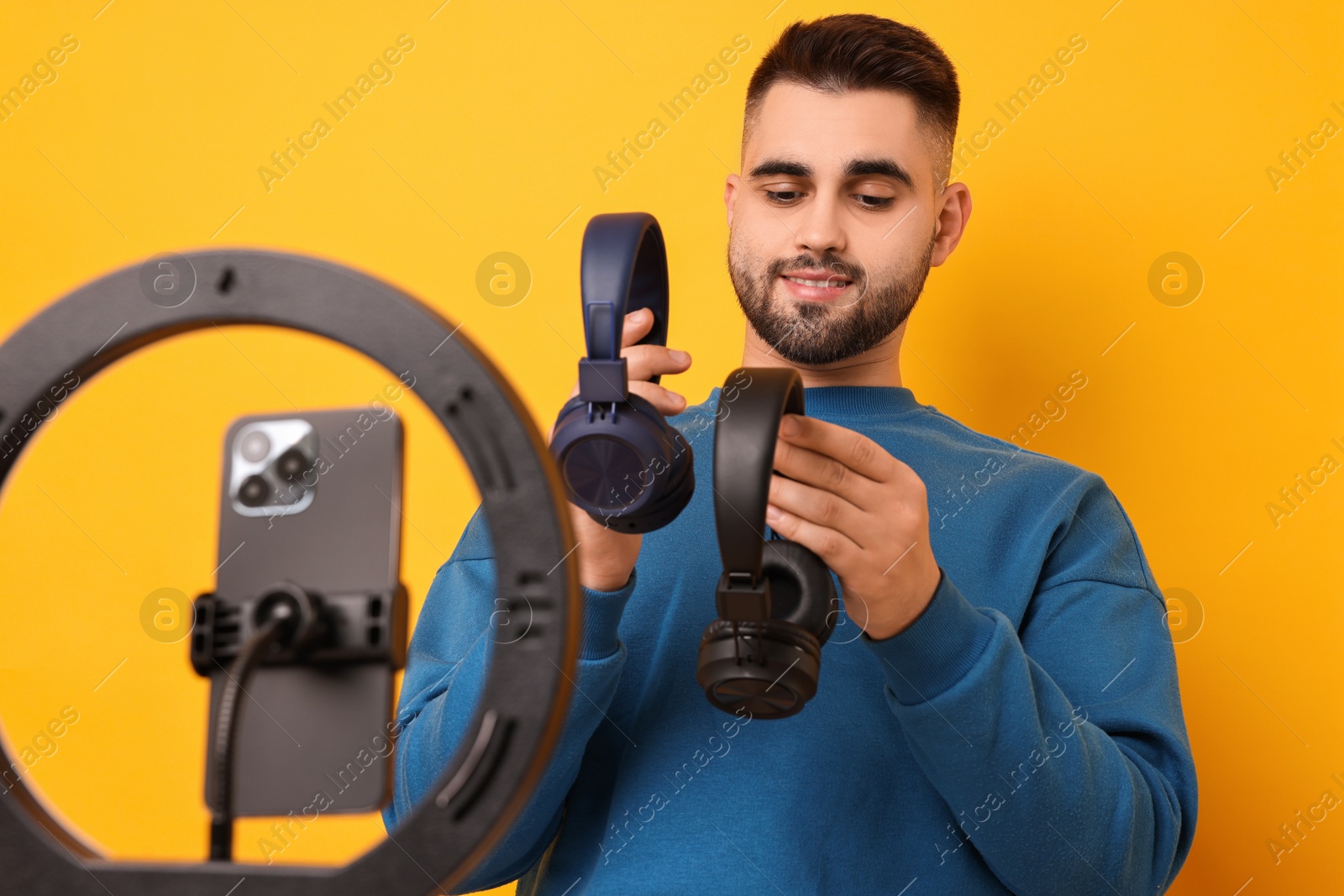 Photo of Technology blogger reviewing headphones and recording video with smartphone and ring lamp on orange background