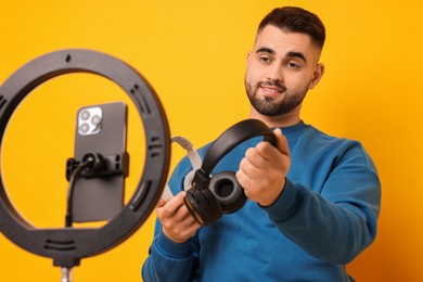 Technology blogger reviewing headphones and recording video with smartphone and ring lamp on orange background