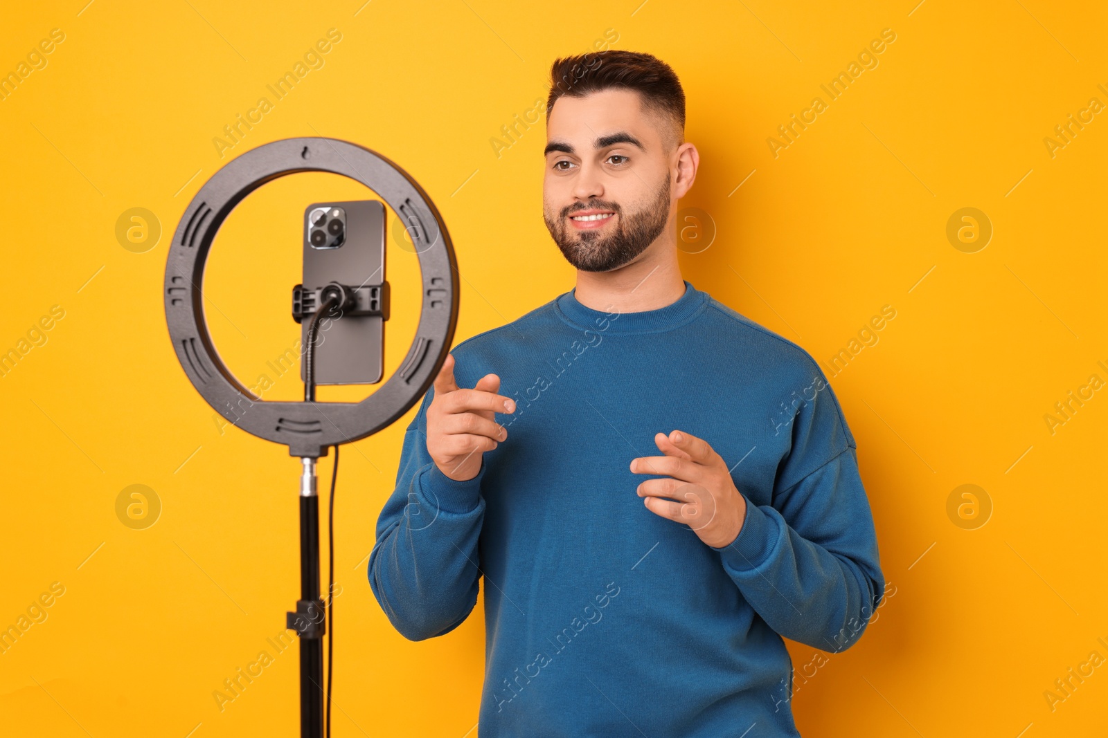 Photo of Blogger recording video with smartphone and ring lamp on orange background