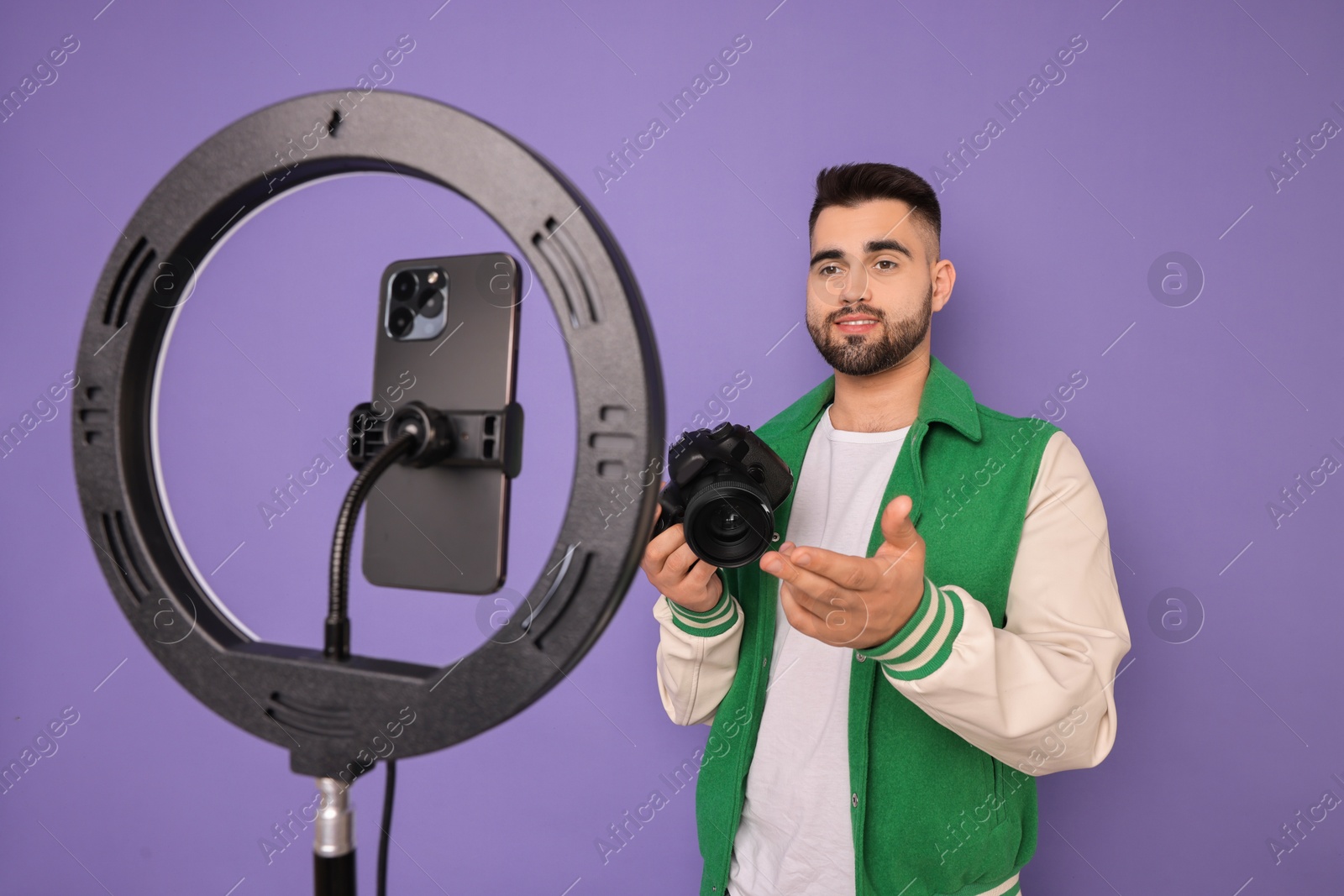 Photo of Technology blogger reviewing camera and recording video with smartphone and ring lamp on purple background