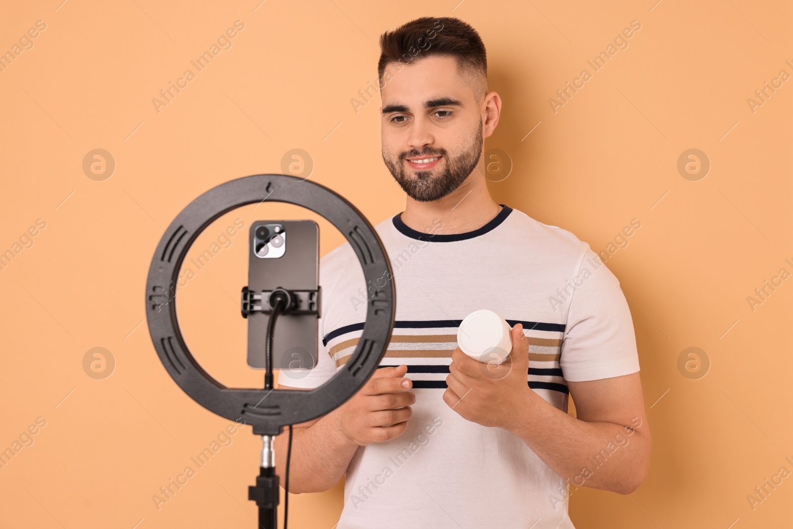 Photo of Beauty blogger reviewing cosmetic product and recording video with smartphone and ring lamp on beige background