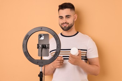 Beauty blogger reviewing cosmetic product and recording video with smartphone and ring lamp on beige background