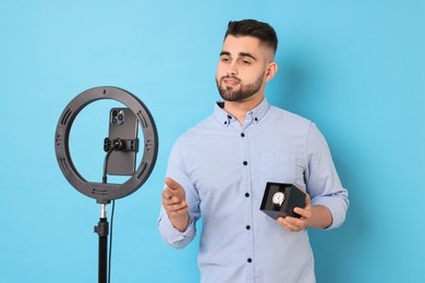Fashion blogger reviewing watch and recording video with smartphone and ring lamp on light blue background