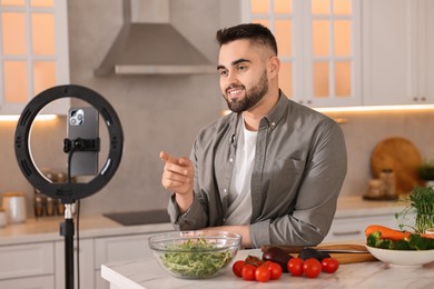 Food blogger cooking while recording video with smartphone and ring lamp in kitchen