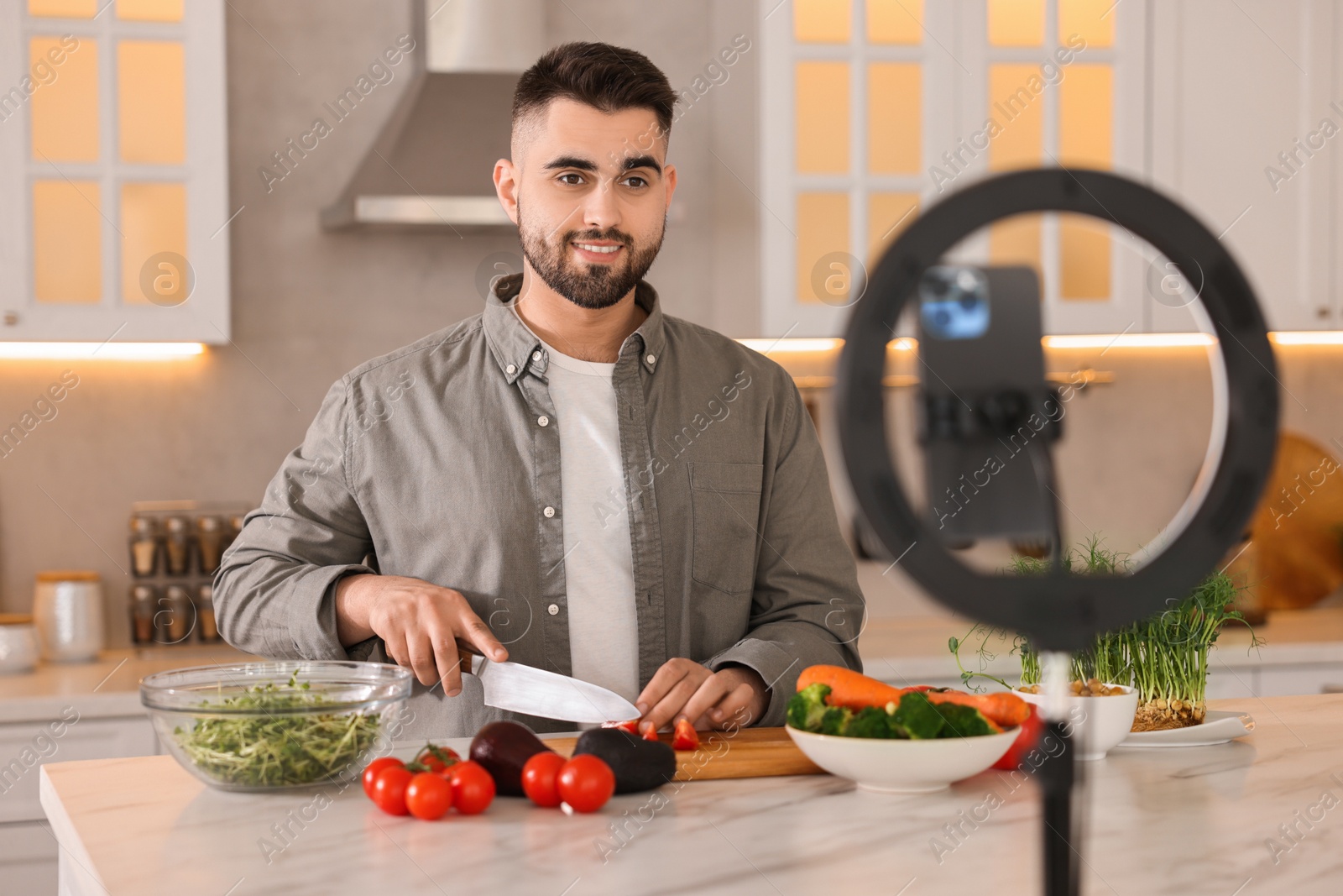 Photo of Food blogger cooking while recording video with smartphone and ring lamp in kitchen