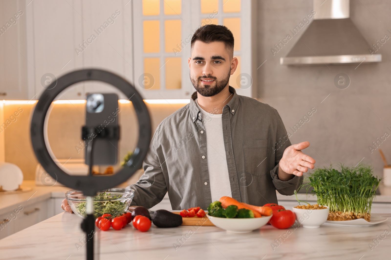 Photo of Food blogger cooking while recording video with smartphone and ring lamp in kitchen