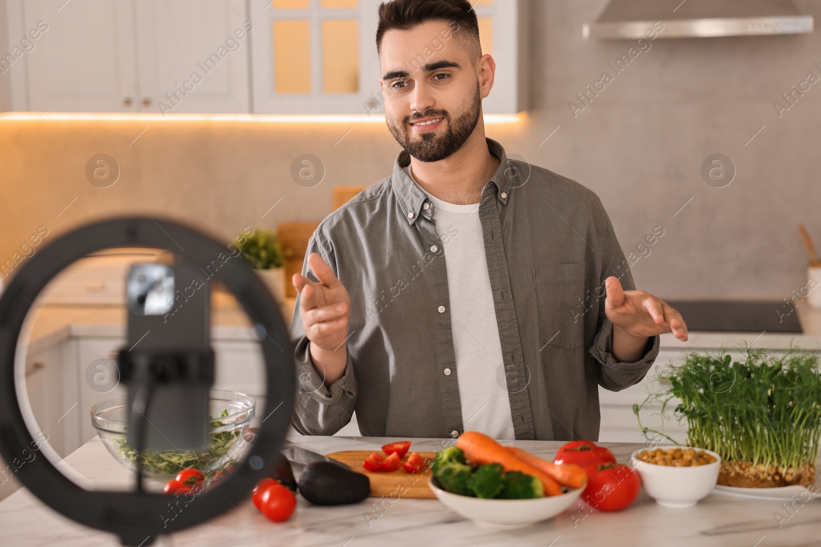 Photo of Food blogger cooking while recording video with smartphone and ring lamp in kitchen