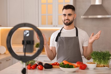 Photo of Food blogger cooking while recording video with smartphone and ring lamp in kitchen